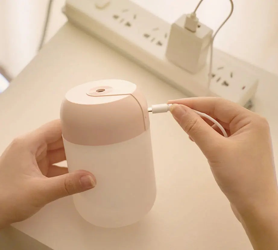 Person plugging a USB cable into a small pink and white device on a light surface.