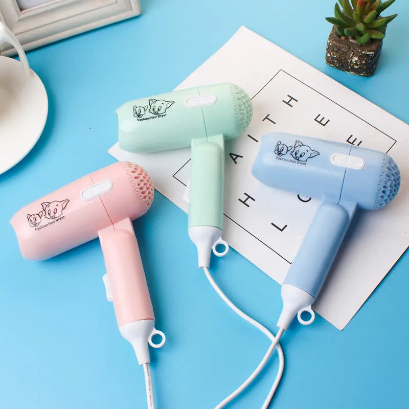 Three small hair dryers in pink, green, and blue on a blue surface with text and a plant in the background.
